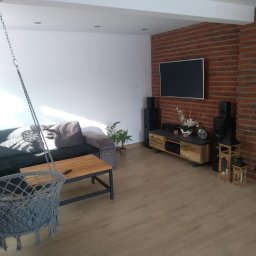 P.H.U Firma Ogólnobudowlana Marek Klinicki - Nowoczesny salon z ceglaną ścianą, wiszącym fotelem, drewnianym stolikiem kawowym i podłogą z paneli w odcieniach beżu, oświetlony światłem dziennym wpadającym przez okno.