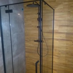 P.H.U Firma Ogólnobudowlana Marek Klinicki - Nowoczesna kabina prysznicowa typu walk-in z czarną armaturą i szklanymi ściankami, wykończona płytkami imitującymi drewno i beton.