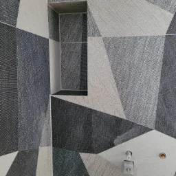 Ściana wyłożona geometrycznymi płytkami w odcieniach szarości i bieli z wnęką i elementami instalacji wodnej.