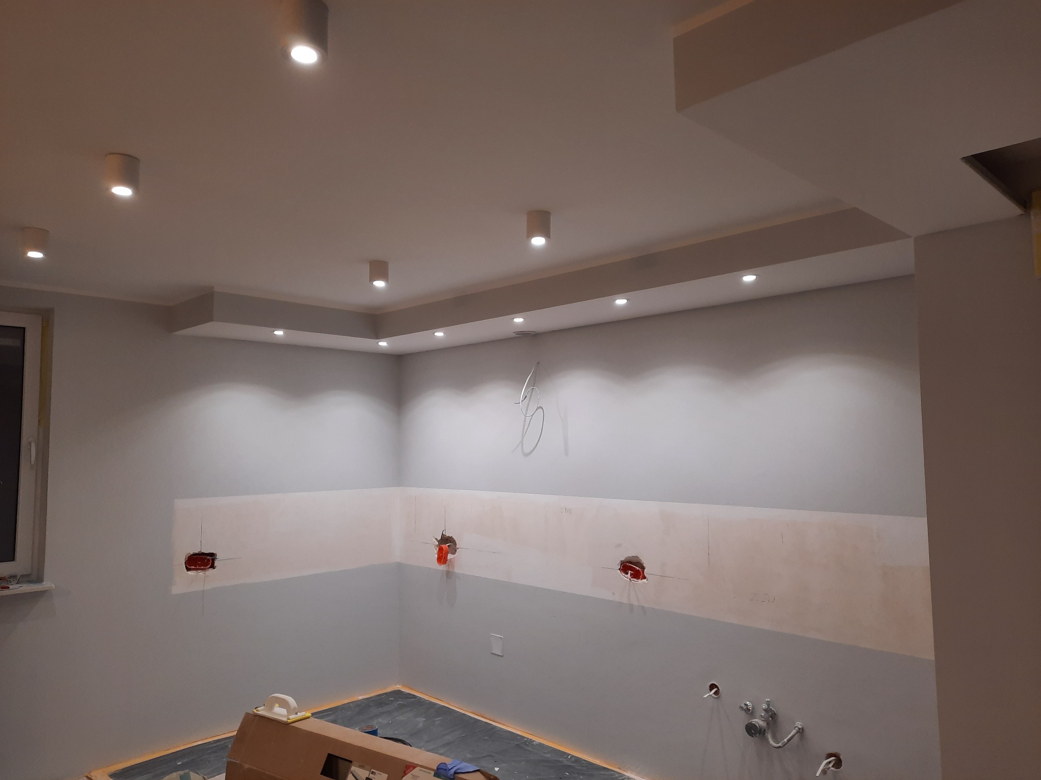 Wnętrze w trakcie remontu: przygotowane ściany pod zabudowę kuchenną z widocznymi puszkami instalacyjnymi, oświetlenie sufitowe typu downlight.