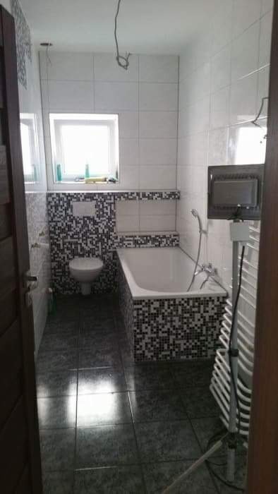 Ukończona łazienka z mozaiką czarno-białą na ścianach i obudowie wanny, szare płytki podłogowe, biała armatura, grzejnik drabinkowy, widoczne niedokończone prace elektryczne.