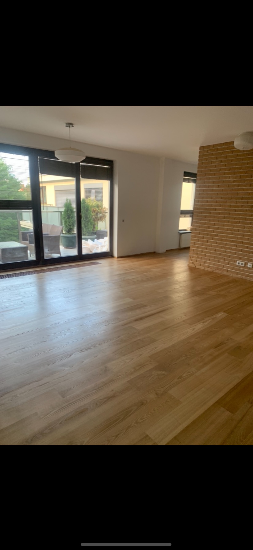 Jasny, drewniany parkiet ułożony w nowym, przestronnym apartamencie z dużymi oknami balkonowymi i ceglaną ścianą.