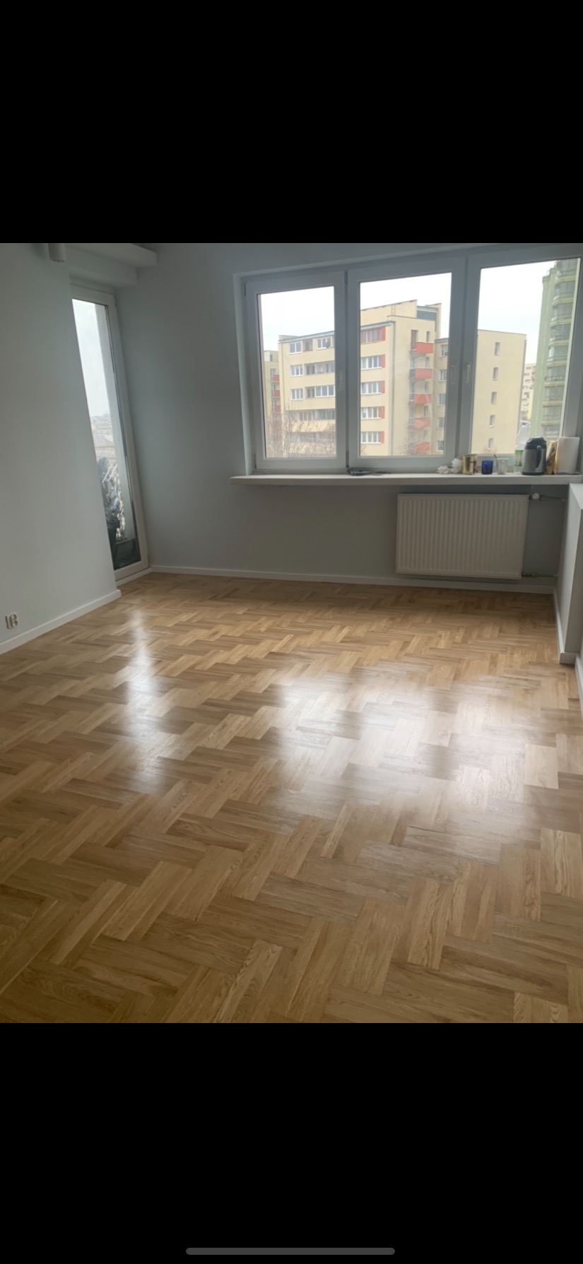 Jasny parkiet ułożony w jodełkę w pustym pokoju z oknem na miasto.