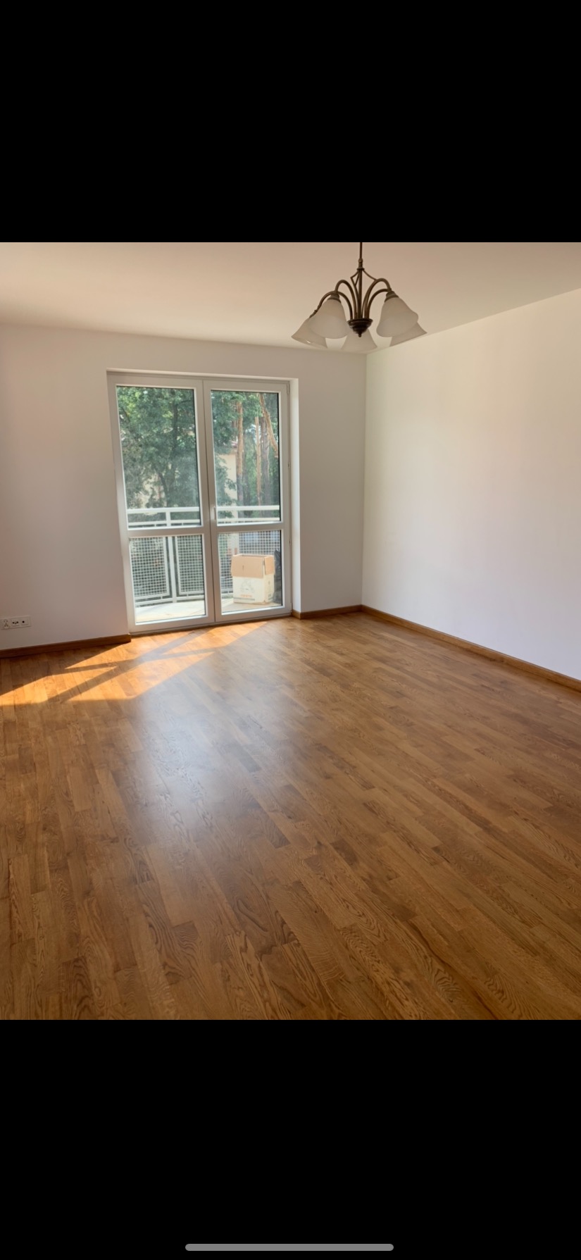 Pokój z odnowioną, lakierowaną podłogą z parkietu dębowego, widoczne ślady światła słonecznego padającego przez balkon.