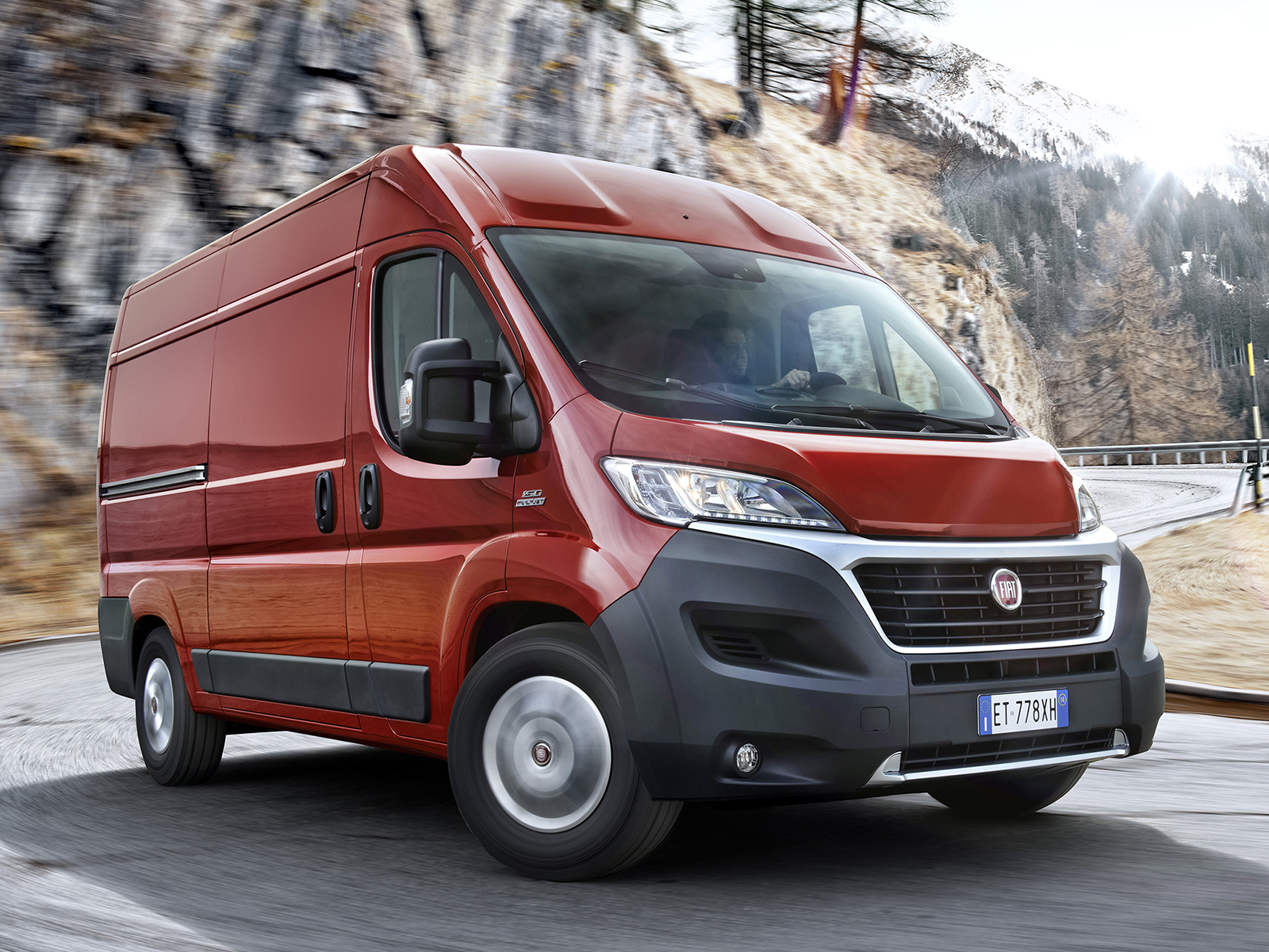 Czerwony Fiat Ducato w ruchu na górskiej drodze, widoczne tablice rejestracyjne ET 778XH oraz ośnieżone zbocza w tle.