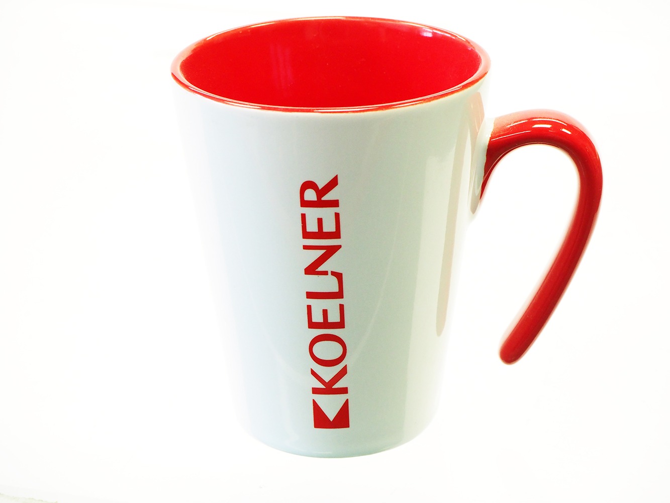 Biały kubek z czerwonym wnętrzem i uchwytem, na którym pionowo nadrukowane jest czerwone logo firmy KOELNER.