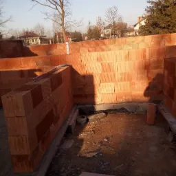 Wznoszenie ścian z czerwonej ceramiki poryzowanej, widoczny poziomica na murze, puszka pianki montażowej, początkowy etap budowy domu.