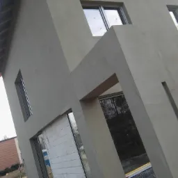 Surowa elewacja domu jednorodzinnego w trakcie prac wykończeniowych, widoczne okna i fragment ściany z bloczków, stan surowy zamknięty.