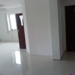 Wnętrze po remoncie: białe ściany, jasna podłoga z płytek, ciemne drewniane drzwi z elementami szkła, widoczne ślady po pracach wykończeniowych przy podłodze.