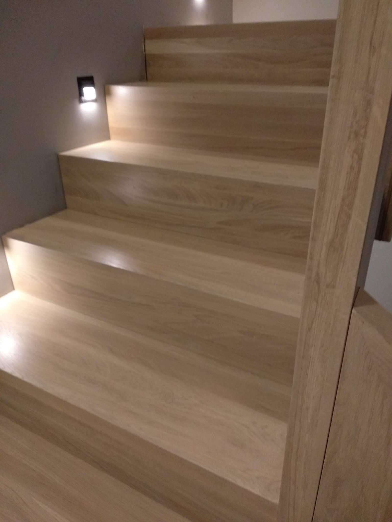 Schody drewniane z oświetleniem punktowym w ścianie, widok z dołu, jasne drewno i minimalistyczny design.