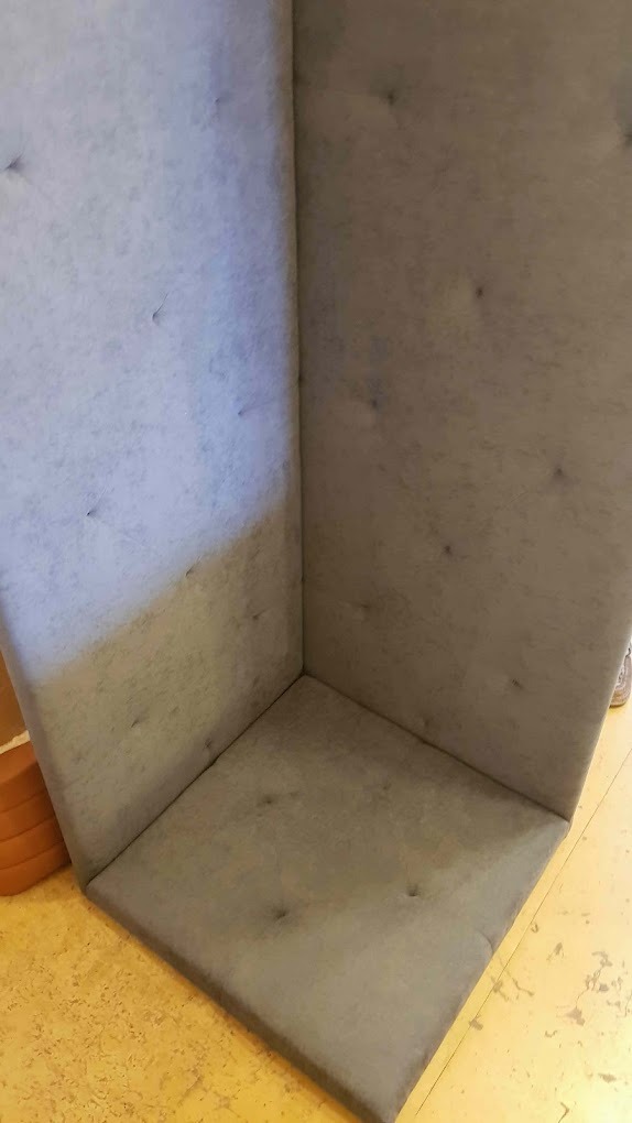 Szary, tapicerowany narożnik z guzikami, widoczny z bliska na tle podłogi z korka.