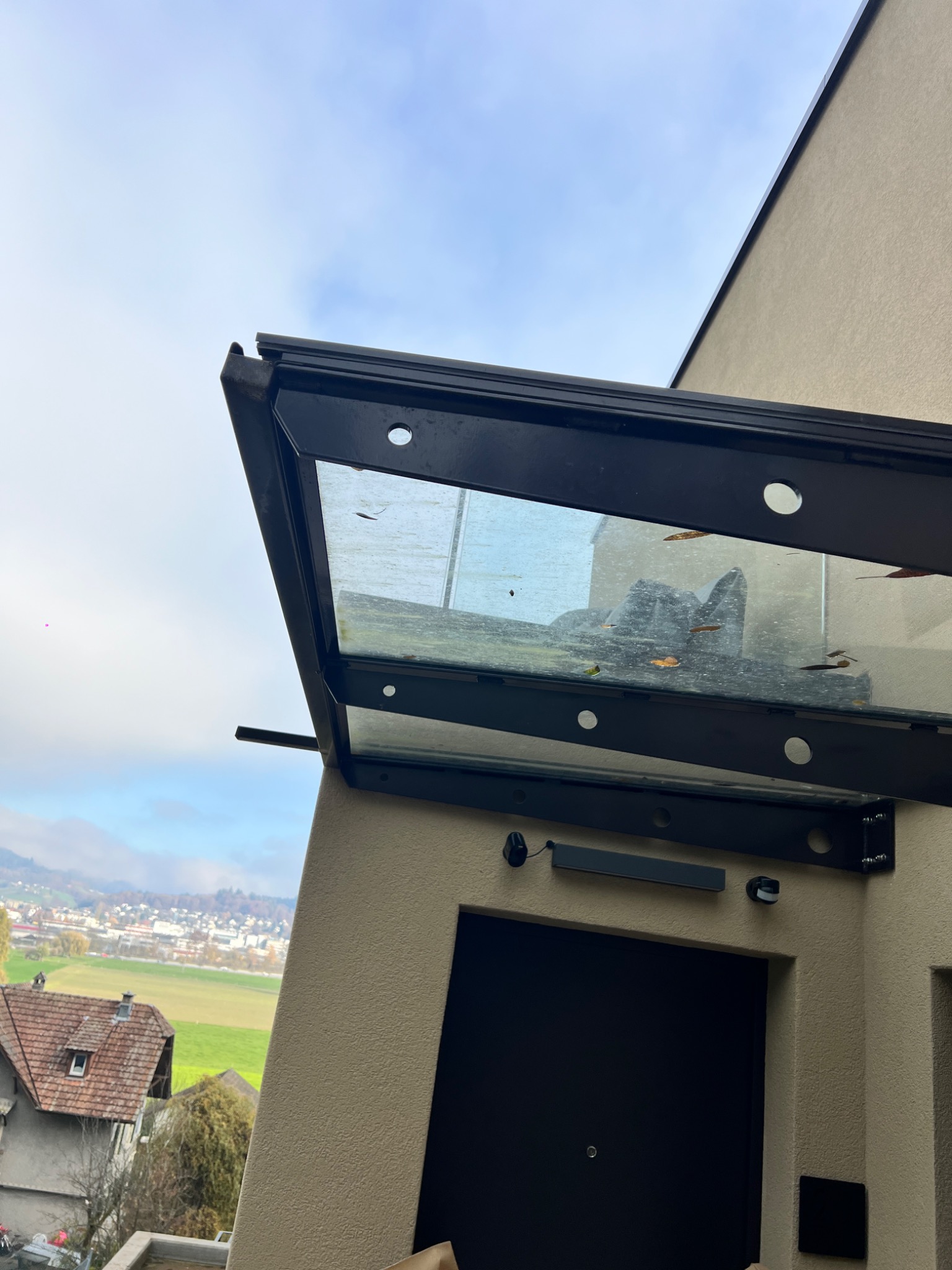 Zadaszenie nad wejściem do budynku w Koszalinie. Konstrukcja metalowa z elementami szklanymi, widok z dołu na tle nieba i zabudowy miejskiej.