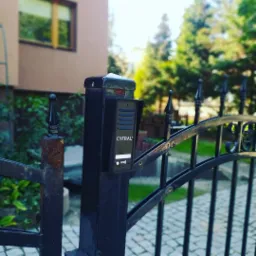 Czarny panel z czytnikiem RFID, zamontowany na słupku bramy wjazdowej, widoczne elementy metalowe z śladami korozji.