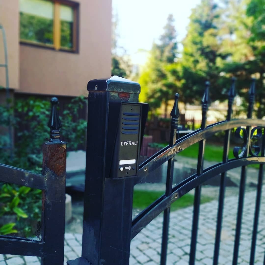 Czarny panel z czytnikiem RFID, zamontowany na słupku bramy wjazdowej, widoczne elementy metalowe z śladami korozji.