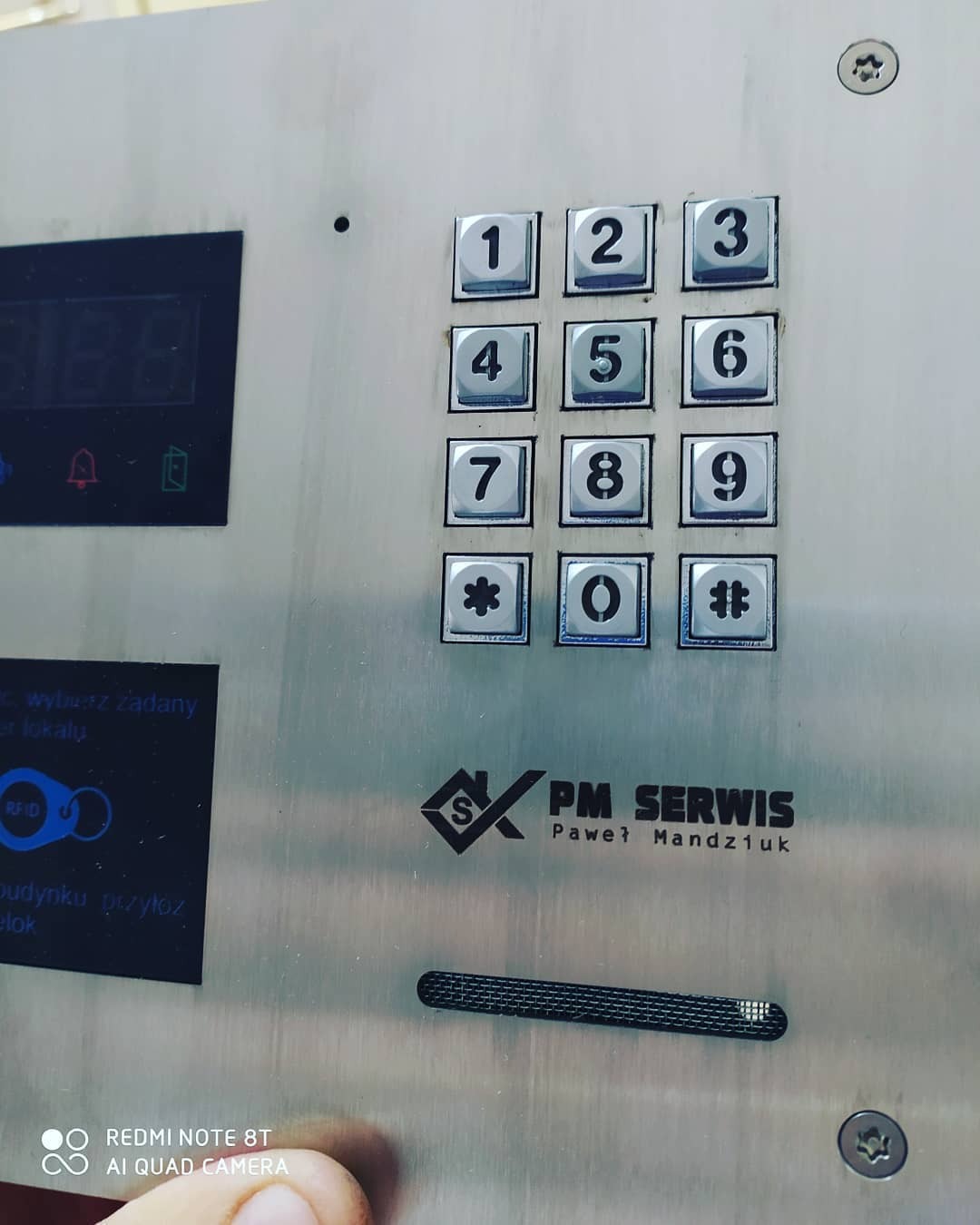 Panel wejściowy z klawiaturą numeryczną i czytnikiem RFID w Głogowie, obok logo firmy PM Serwis.