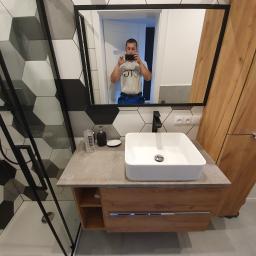 OTGlazurnik Małopolska Oskar Tracz - Nowoczesna łazienka z heksagonalnymi płytkami w odcieniach szarości i bieli, czarną armaturą, umywalką nablatową i szafką z drewnopodobnym frontem, widoczny autor zdjęcia w lustrze.