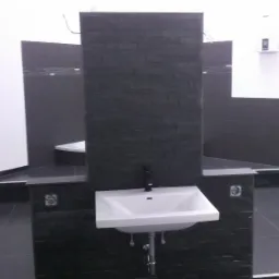 Nowoczesna łazienka z czarnymi płytkami imitującymi kamień na ścianie za białą umywalką z czarną baterią, widoczny fragment kabiny prysznicowej i wanny.