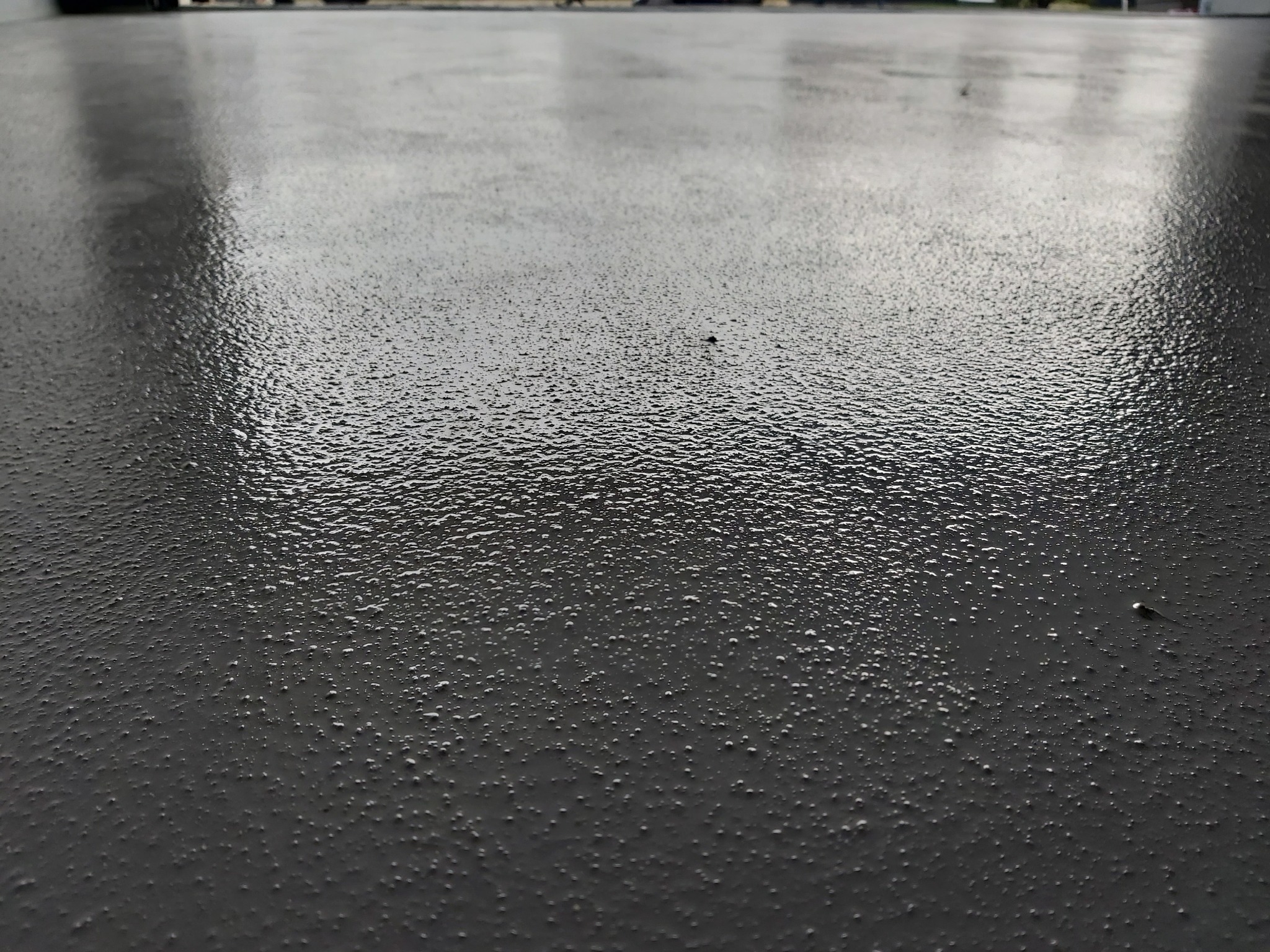 Szara, błyszcząca powierzchnia podłogi z widoczną teksturą i refleksami świetlnymi.