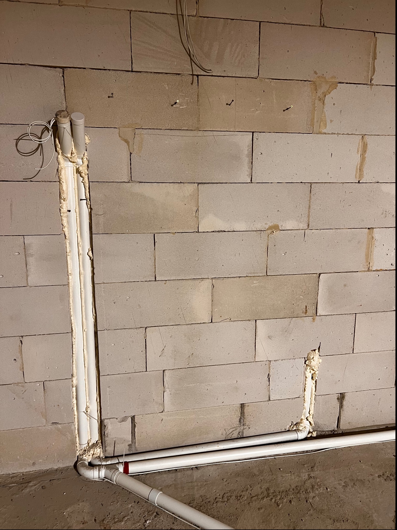 Instalacja rur w bruździe w ścianie z bloczków, zabezpieczona pianką montażową, widoczne przewody elektryczne i fragment podłogi.