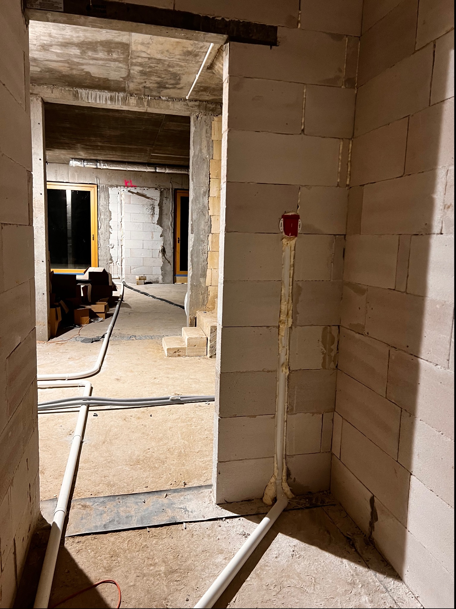 Wnętrze w trakcie instalacji przewodów i gniazd elektrycznych w surowym stanie, widoczne białe ściany z betonu komórkowego, podłoga wylewka, wystające przewody i rury, puszka elektryczna...