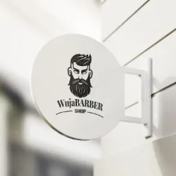Okrągły szyld z logo 'WujaBARBER SHOP' przedstawiającym stylizowaną twarz brodatego mężczyzny z modną fryzurą, zamocowany na białej ścianie z poziomymi panelami.