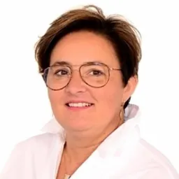 Portret kobiety w okularach i białej koszuli, uśmiechającej się do kamery, na jasnym tle.