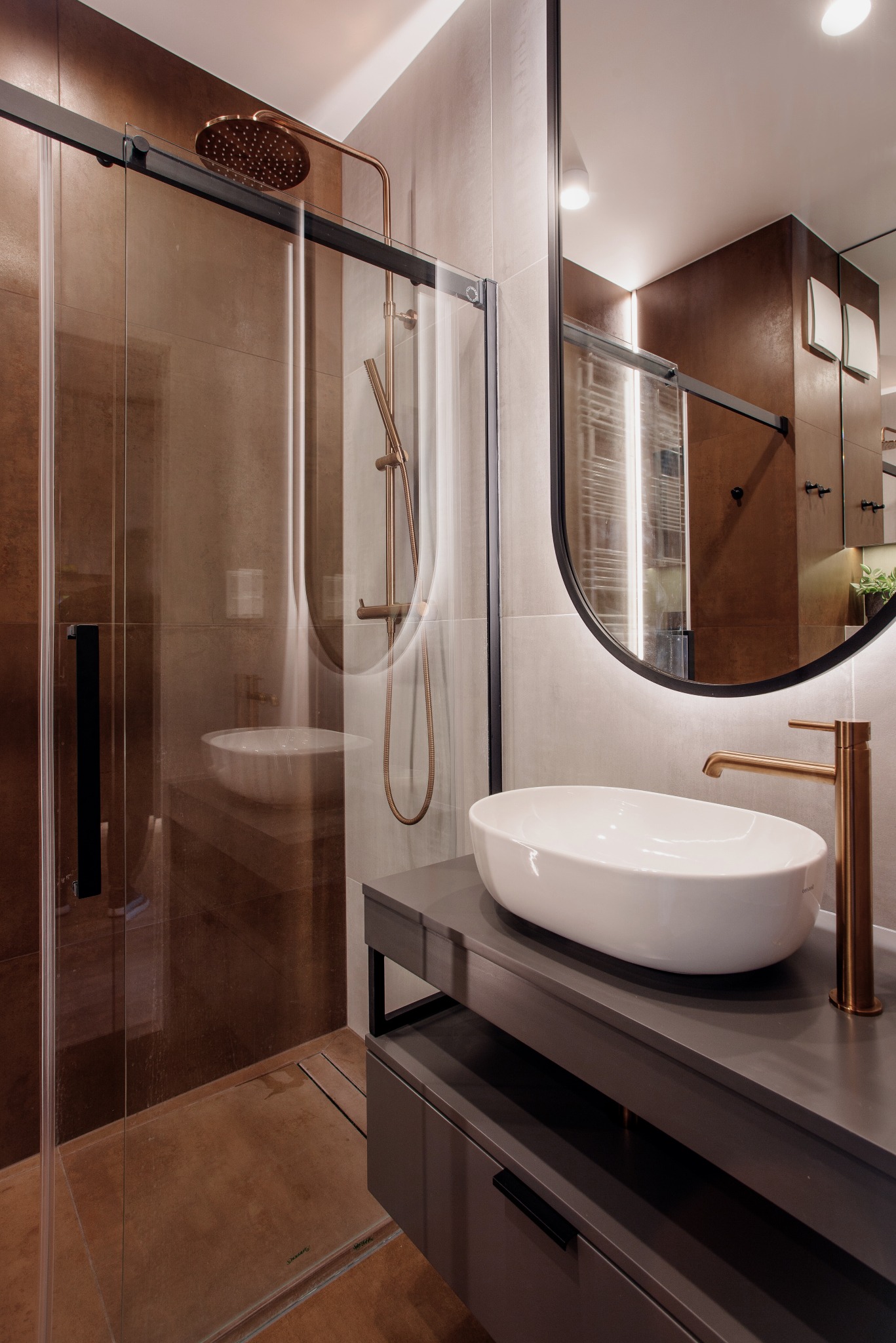 Nowoczesna łazienka z kabiną prysznicową typu walk-in, umywalką nablatową i lustrem z podświetleniem LED. Armatura w kolorze miedzi.