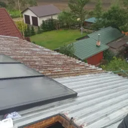 Montaż paneli solarnych na metalowym dachu, widok z góry na częściowo zamontowane panele, z widocznym krajobrazem w tle.