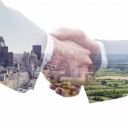 Uścisk dłoni z nałożonymi panoramami miasta i terenów zielonych, symbolizujący partnerstwo i zrównoważony rozwój.