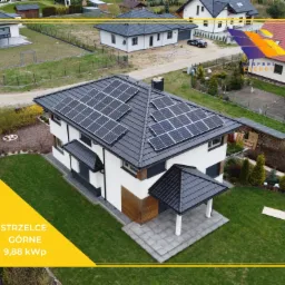 Instalacja paneli słonecznych na dachu dwukondygnacyjnego domu w Strzelcach Górnych, widok z góry, panele ułożone w kilku rzędach, ciemna dachówka, biała elewacja z drewnianymi akcentami.