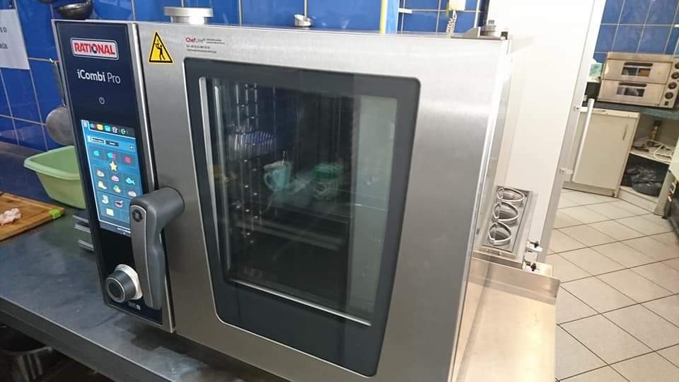 Profesjonalny piec konwekcyjno-parowy Rational iCombi Pro z dotykowym panelem sterowania, widoczne naczynia wewnątrz, w tle niebieskie płytki i wyposażenie kuchenne.