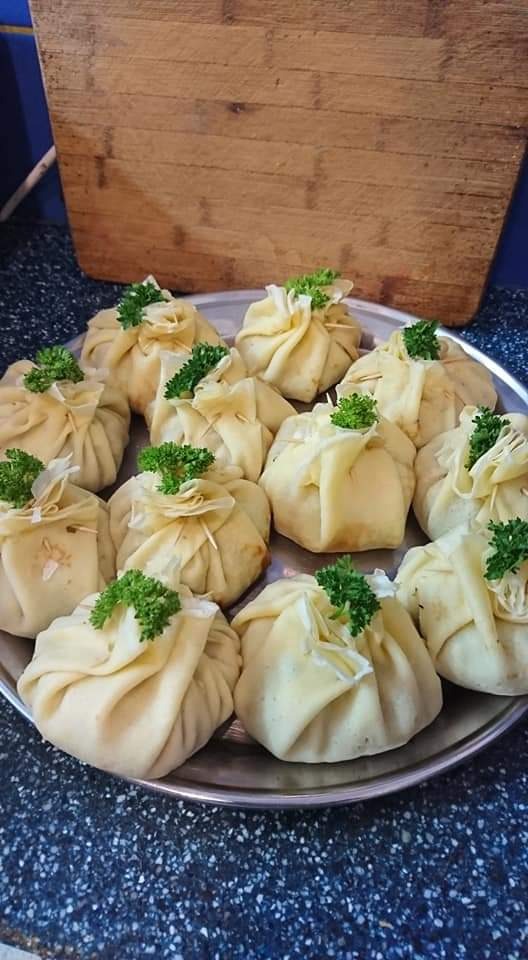 Słoneczne naleśniki zawinięte w sakiewki, przewiązane ciastem i udekorowane świeżą pietruszką, ułożone na srebrnej tacy.