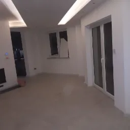 Wnętrze nowocześnie wykończonego salonu z kominkiem, białymi ścianami, jasną podłogą, oświetleniem LED na suficie i systemem alarmowym na ścianie obok kominka.