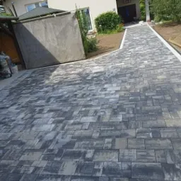 Ułożona kostka brukowa w Myślenicach tworząca ścieżkę i podjazd przed domem, z widocznymi obrzeżami i elementami krajobrazu.