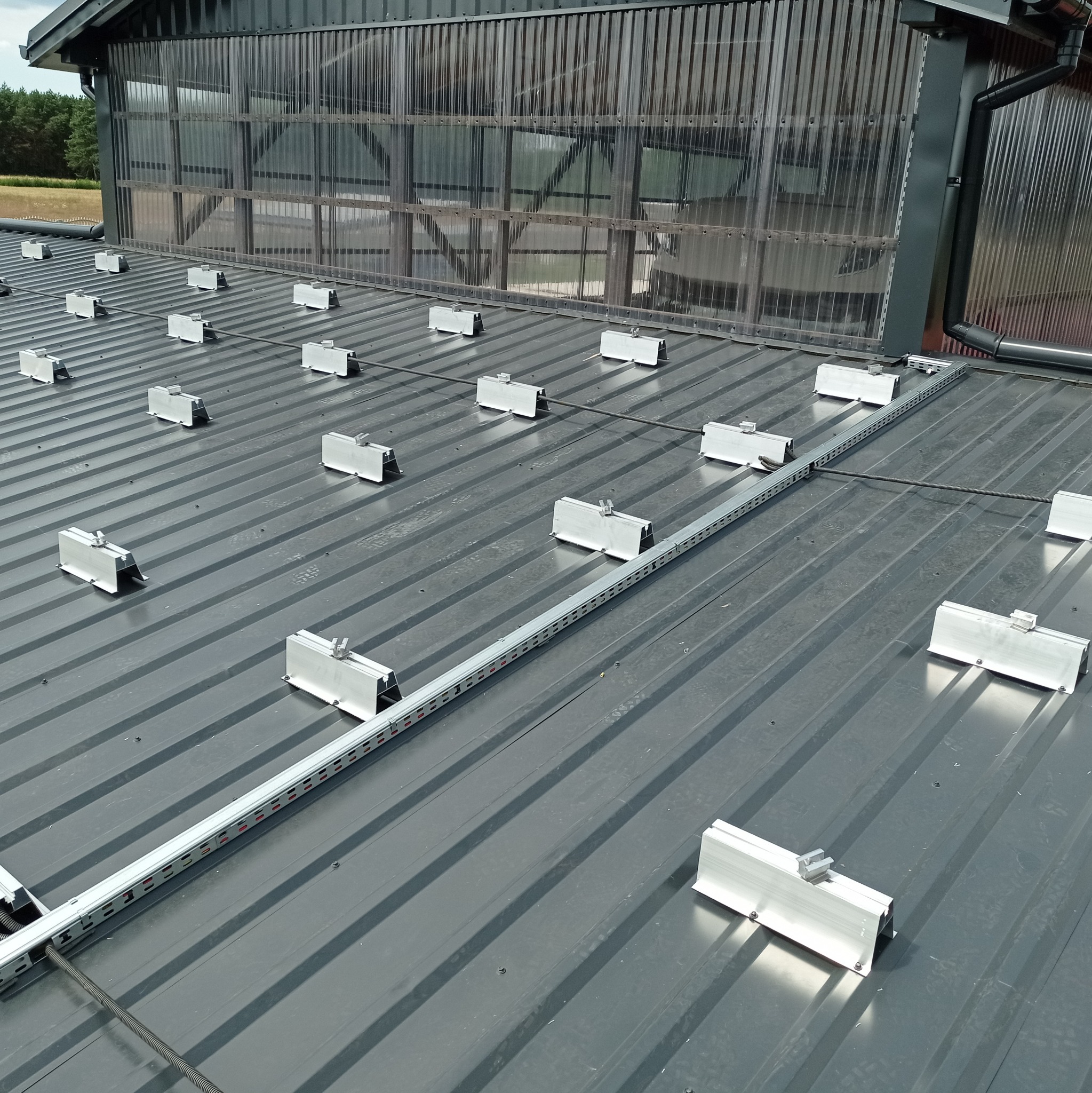 Metalowy dach z zamontowanymi uchwytami i szynami montażowymi pod panele słoneczne, widoczne elementy konstrukcji budynku.