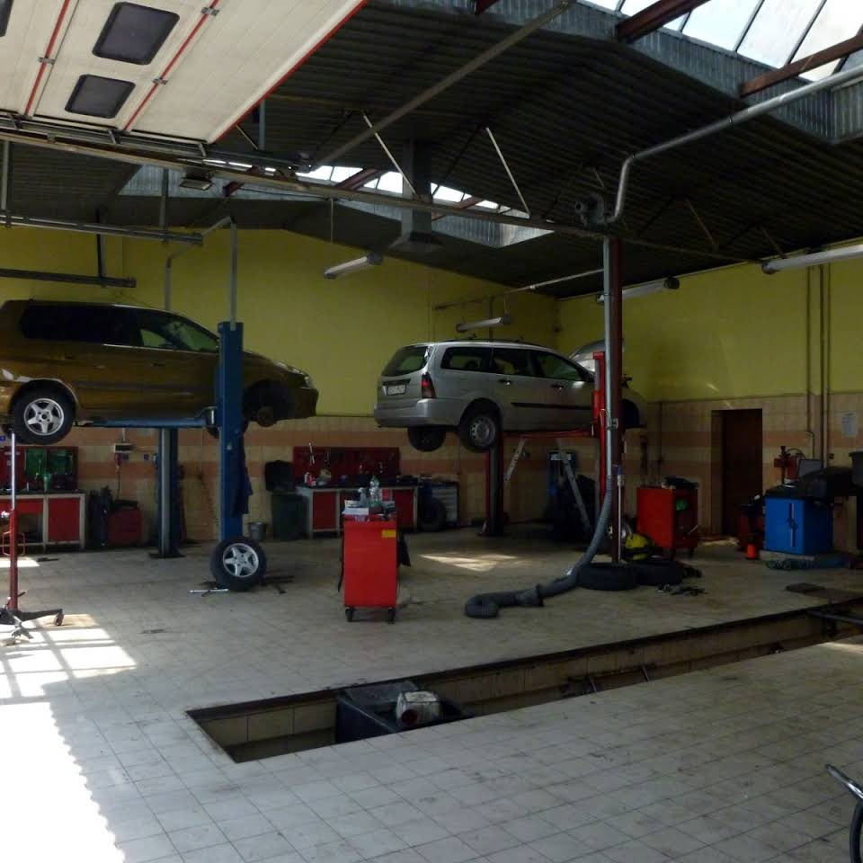 Wnętrze warsztatu samochodowego w Starogardzie Gdańskim z dwoma samochodami uniesionymi na podnośnikach; widoczny kanał rewizyjny w posadzce.