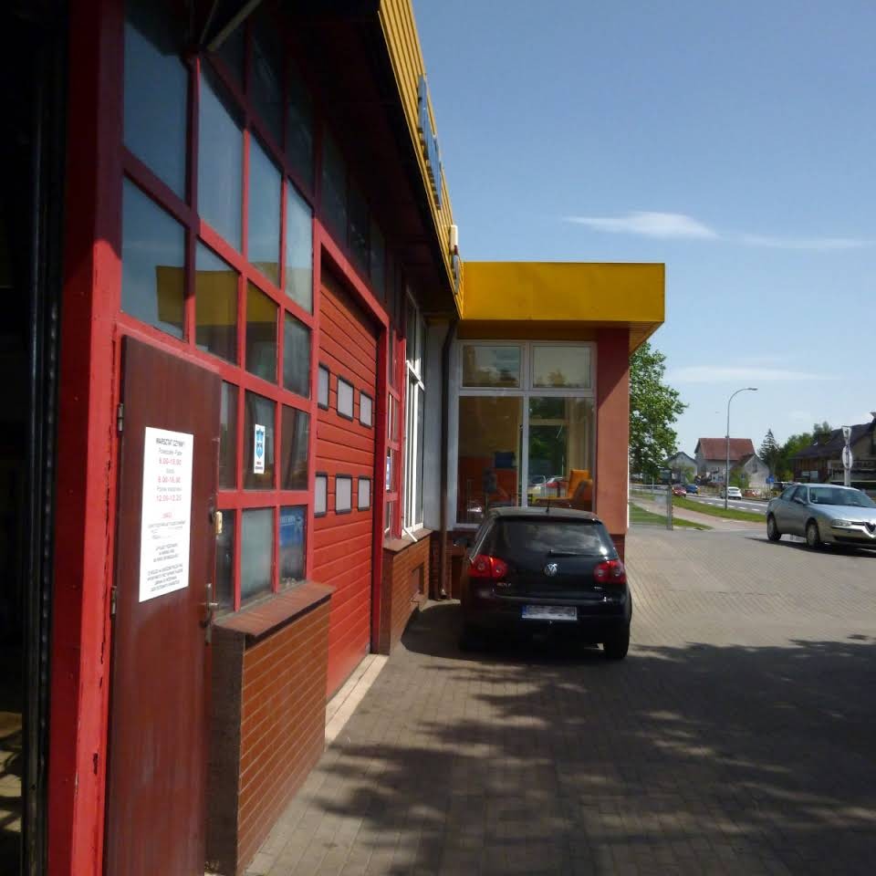 Czerwono-żółty budynek warsztatu samochodowego z zaparkowanym czarnym Volkswagenem Golfem przed wejściem.