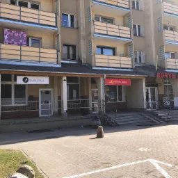 Fasada budynku z biurami: 'Na Obcasach' biuro rachunkowe, Poczta Polska i 'Borys Monopolowy', z balkonami i rozwieszonym praniem w serduszka