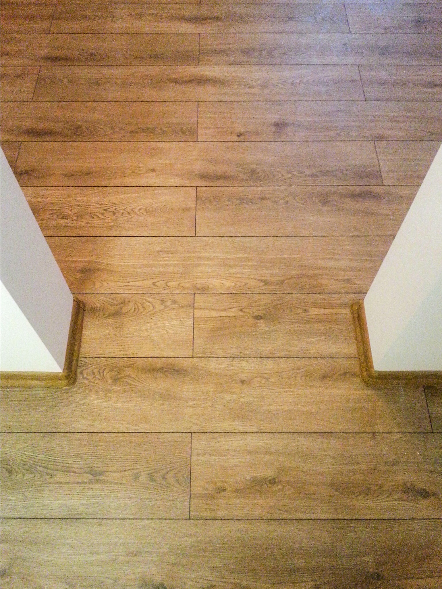 Ułożony parkiet z jasnego drewna, widoczne białe narożniki ścian z brązowymi listwami przypodłogowymi.