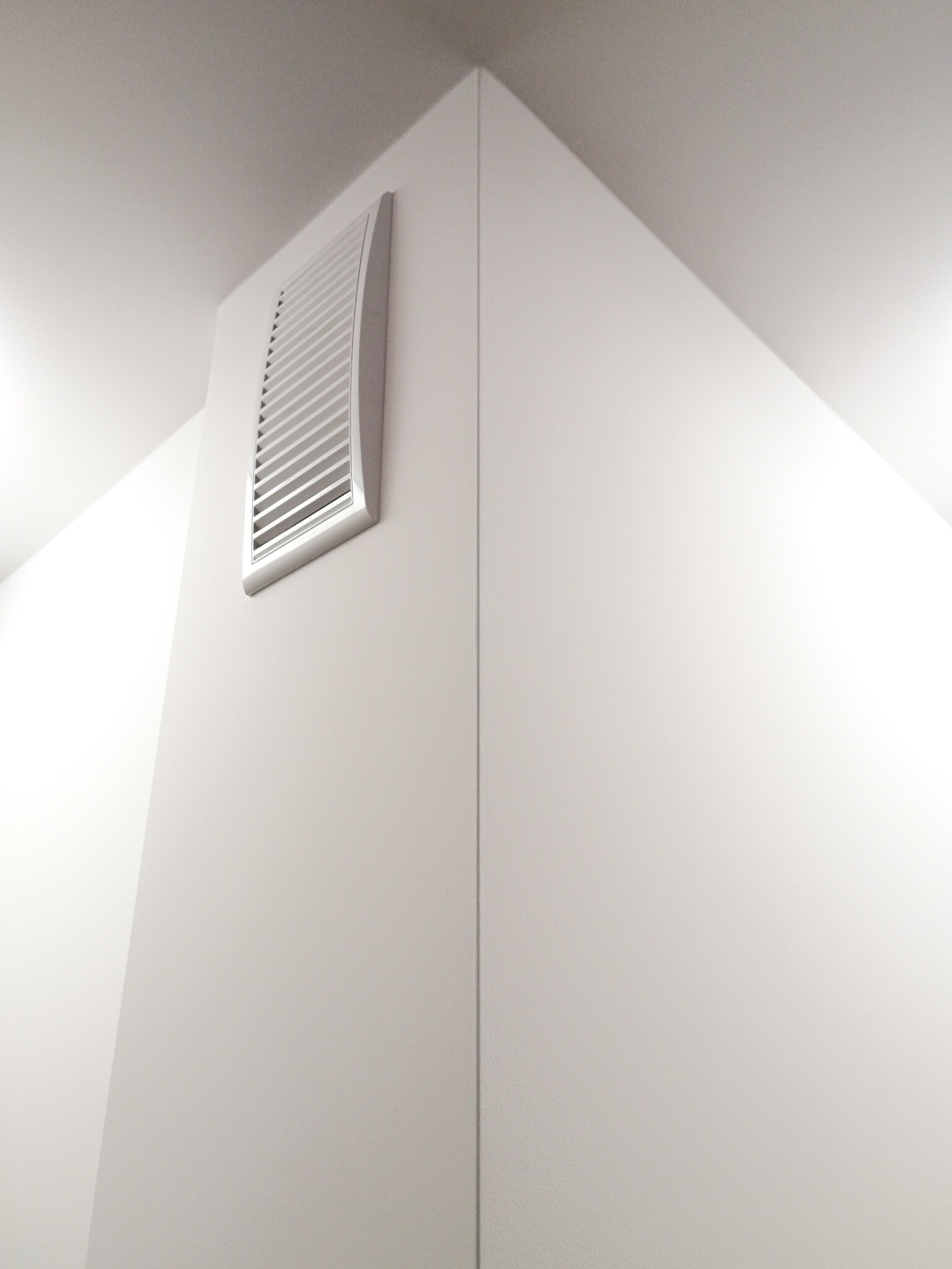 Biała kratka wentylacyjna z poziomymi szczelinami, zamontowana w rogu ściany i sufitu, świeżo po malowaniu.
