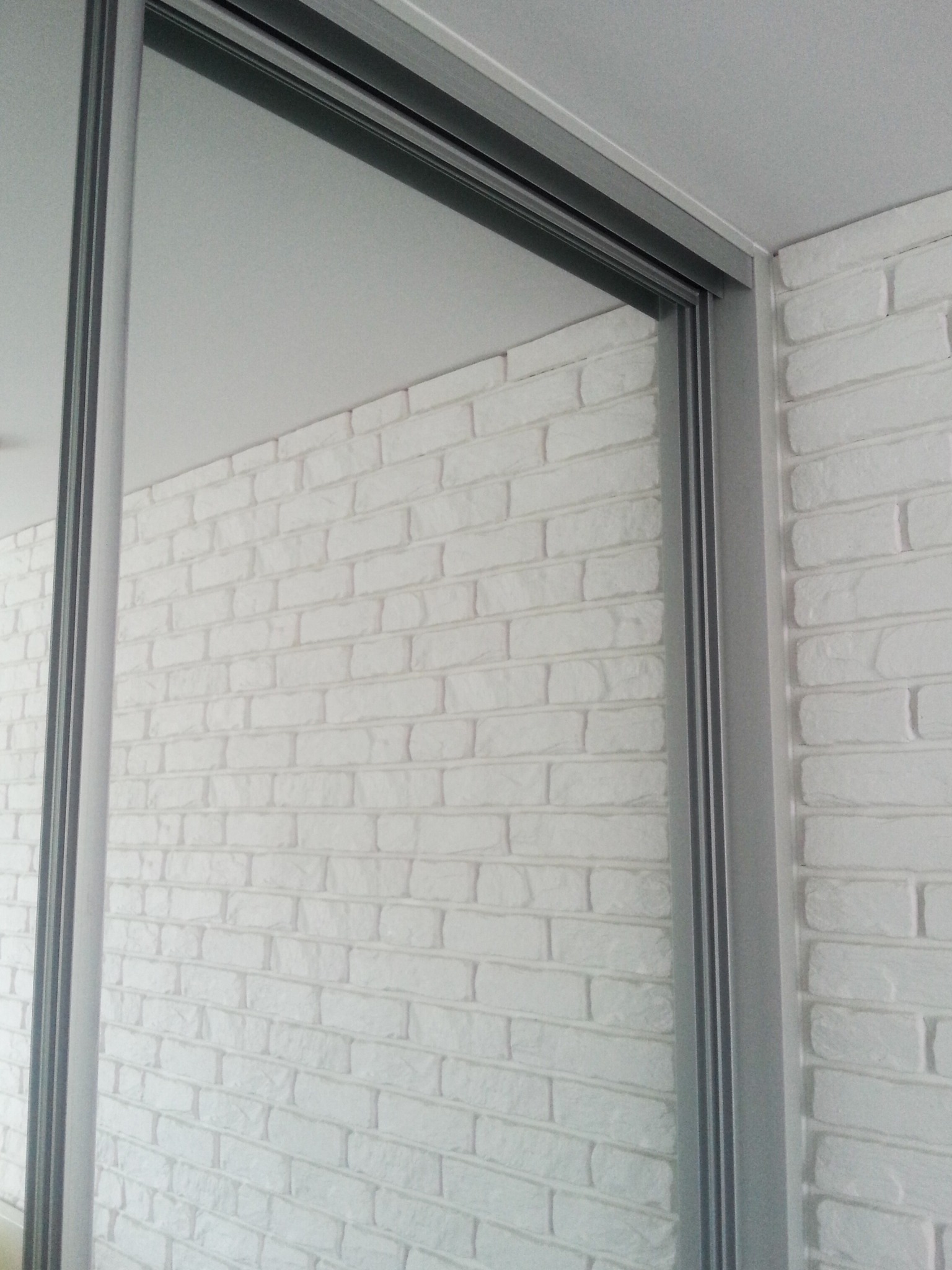 Zamknięte drzwi przesuwne z lustrem w metalowej ramie, przylegające do ściany wyłożonej białą cegłą dekoracyjną.