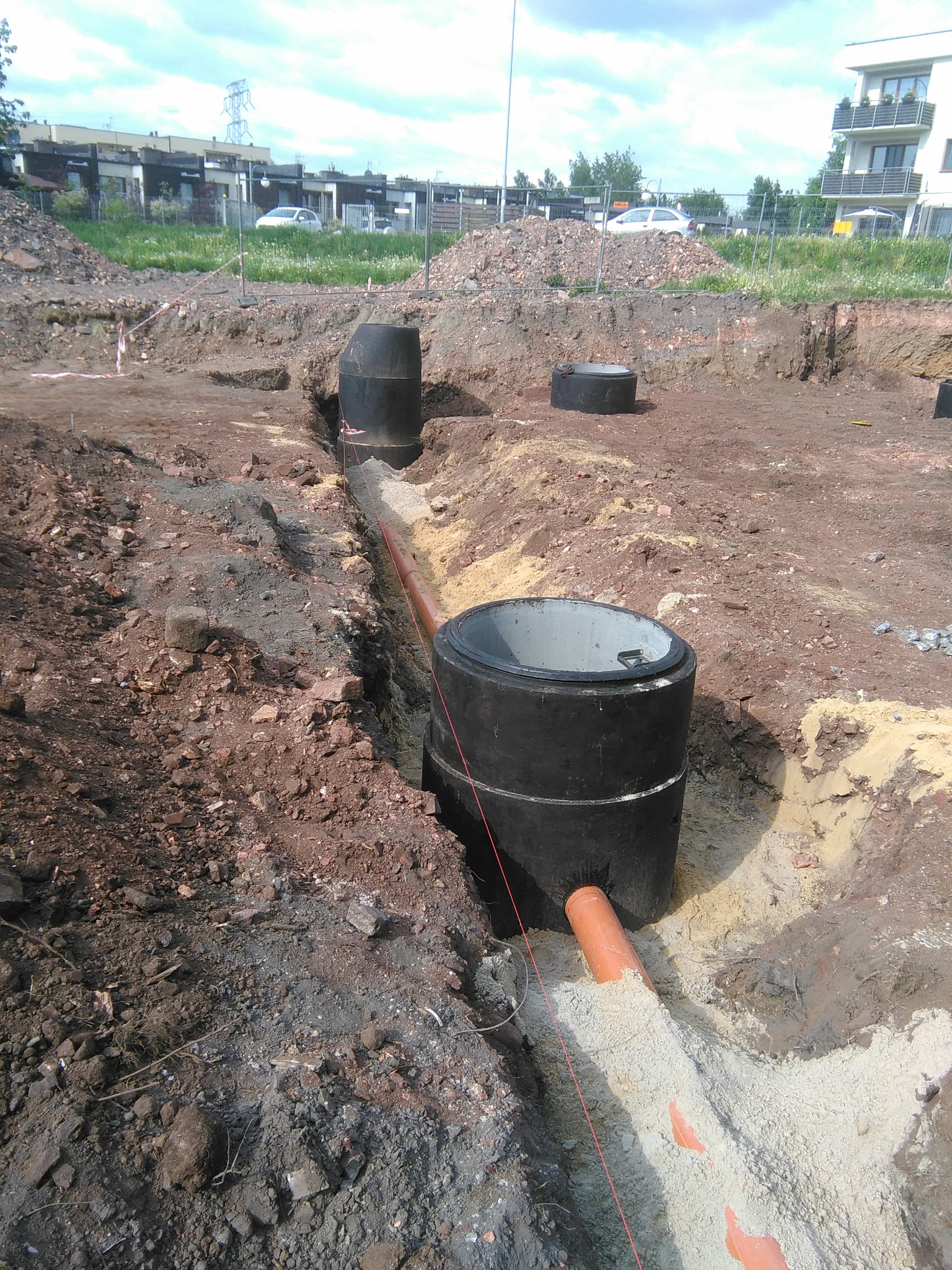 Wykop z ułożoną rurą kanalizacyjną w piaskowej podsypce, widoczne betonowe studzienki kanalizacyjne w trakcie montażu, teren budowy w Chorzowie.
