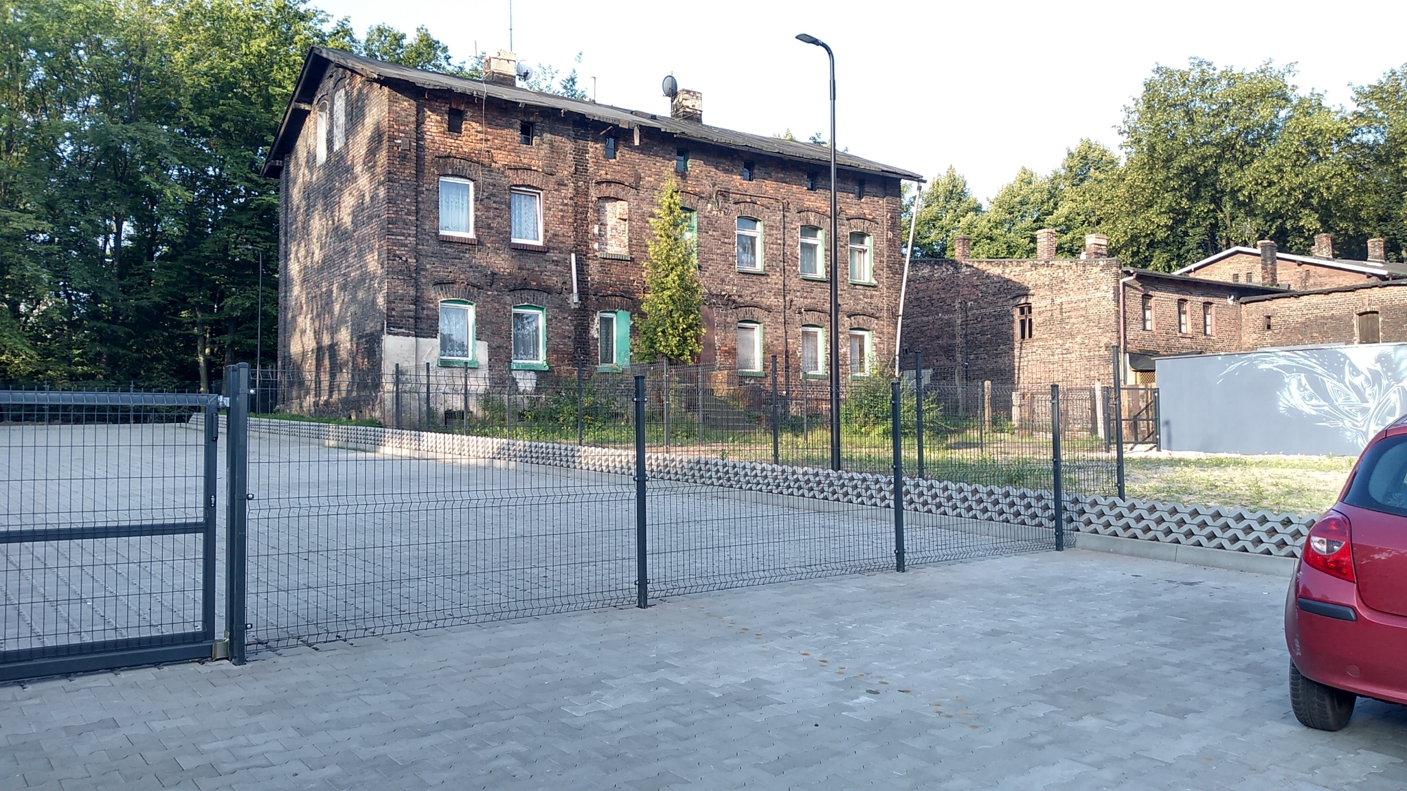 Nowoczesne ogrodzenie panelowe z siatki z bramą wjazdową, zabezpieczające parking przed ceglanym budynkiem w Rudzie Śląskiej.