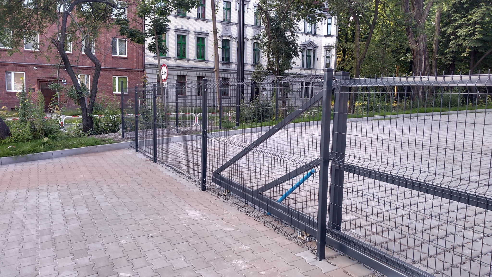 Metalowe ogrodzenie panelowe z bramą przesuwną, zabezpieczające parking w Rudzie Śląskiej, widoczne budynki mieszkalne w tle.