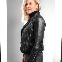 Studio Fotograficzne Laura Bąk - Portret kobiety w czarnej skórzanej kurtce na jasnym tle. Blond włosy, delikatny uśmiech, profesjonalna sesja w studio z oświetleniem podkreślającym kontury.