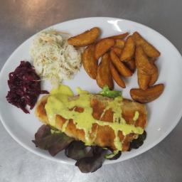 Fabryka Smaków Legionowo - Biały talerz z panierowaną rybą polaną sosem, frytkami z ziemniaków, surówką z kapusty i buraczkami na tle metalowego blatu.