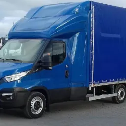 Niebieski samochód dostawczy Iveco z plandeką na parkingu, widoczny znak Fiat w tle.