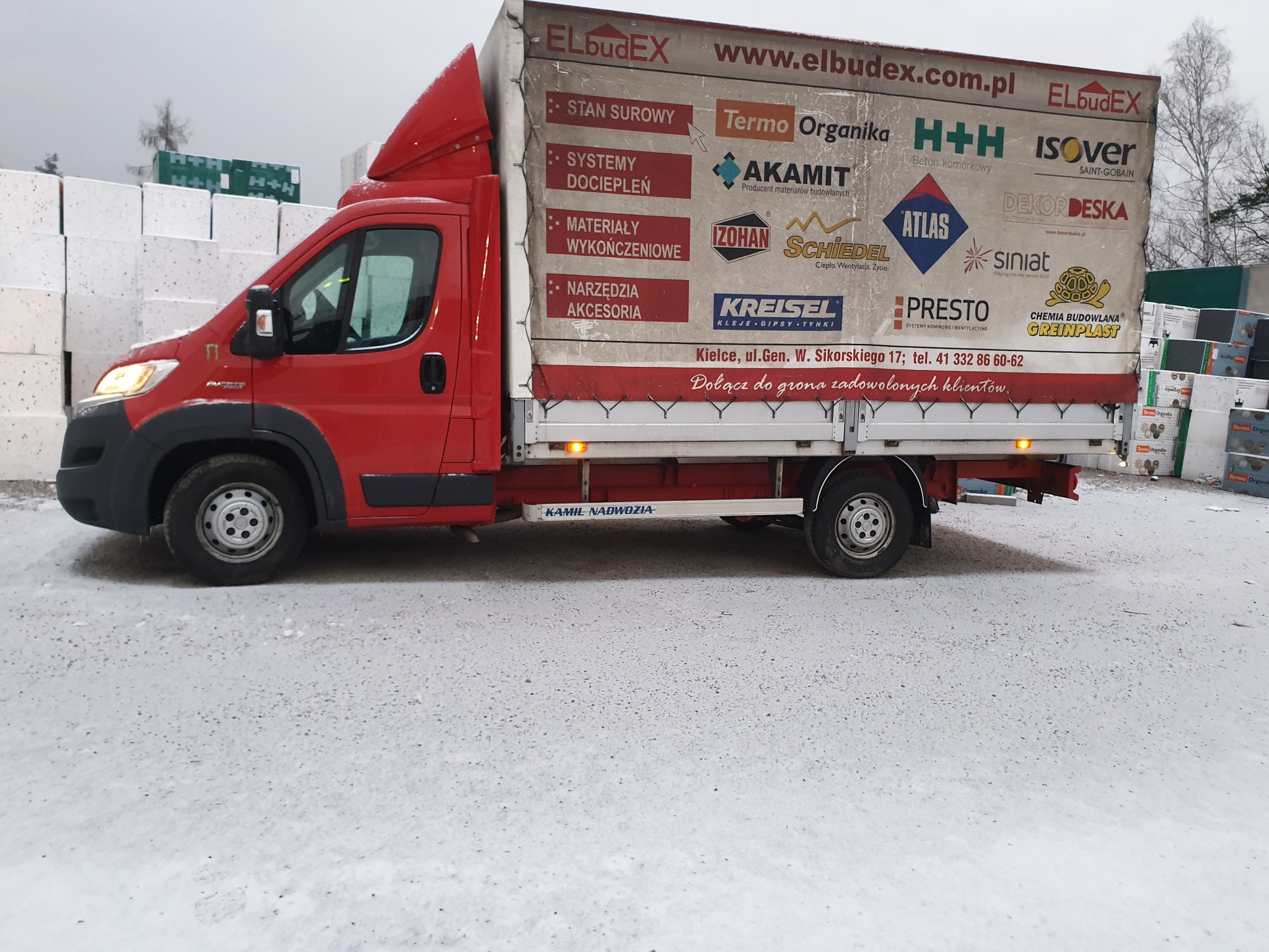 Czerwony samochód dostawczy z reklamą materiałów budowlanych na białym tle śniegu, widok z boku.