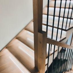 Sławomir Tytuła Usługi stolarskie - Nowoczesne schody drewniane z podświetleniem LED stopni i czarnymi, metalowymi balustradami, widok z góry na dół, jasne drewno.