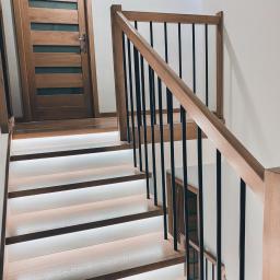 Sławomir Tytuła Usługi stolarskie - Nowoczesne schody drewniane z podświetlanymi stopniami i czarnymi balustradami, widoczne drzwi z drewnianą ramą i szybami.